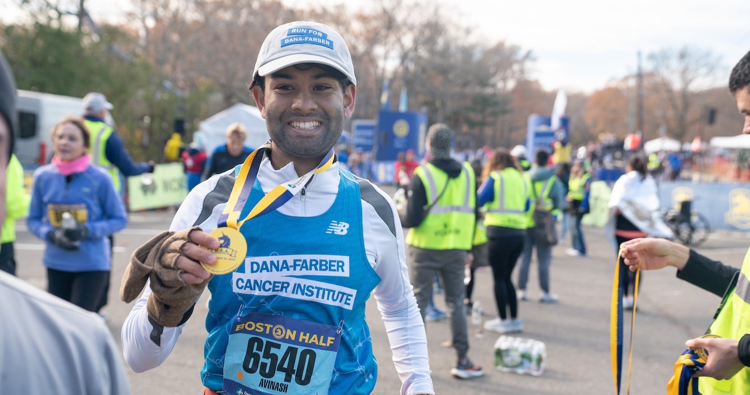 A runner in Dana-Farber gear holding his Boston Half finisher’s medal