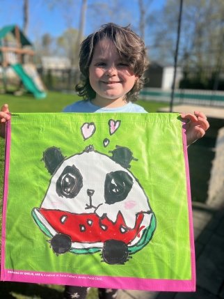 Young girl holding a green reusable tote featuring a panda eating watermelon