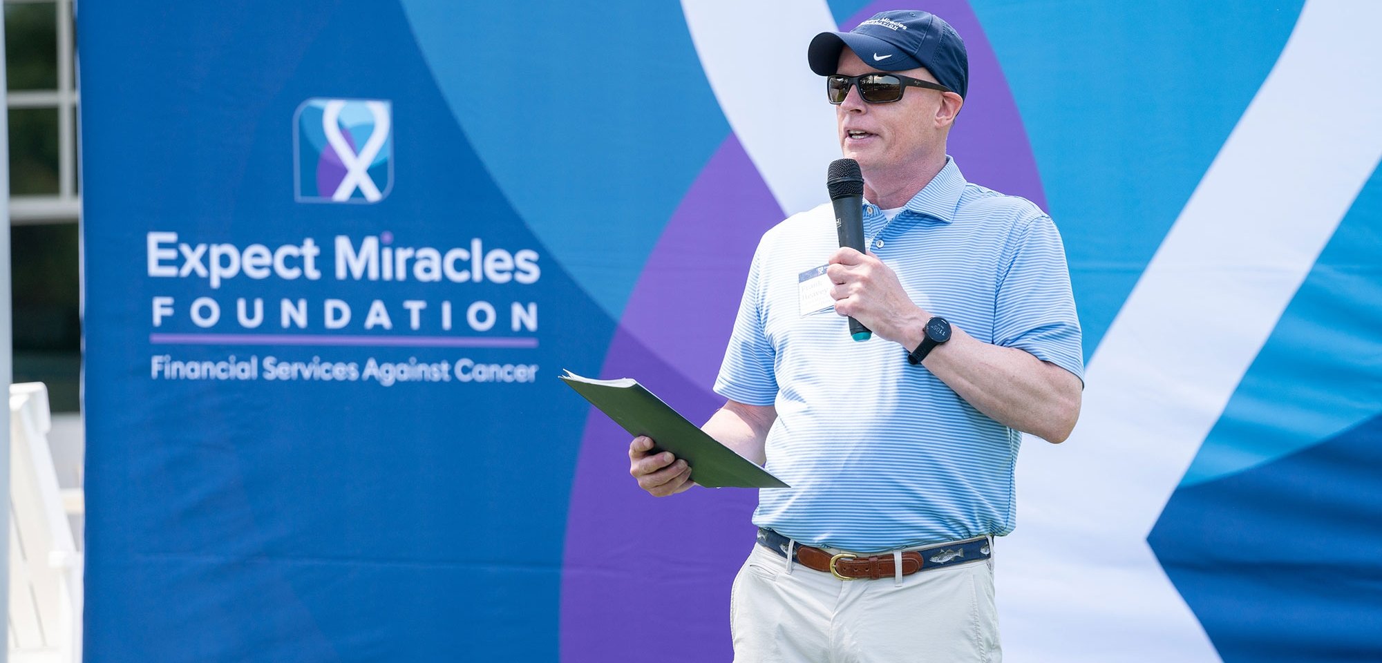 Man speaking into a microphone in front of an Expect Miracles Foundation backdrop