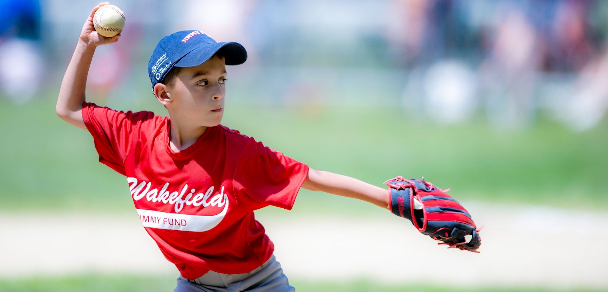 Little League player throwing a ball wearing Jimmy Fund gear