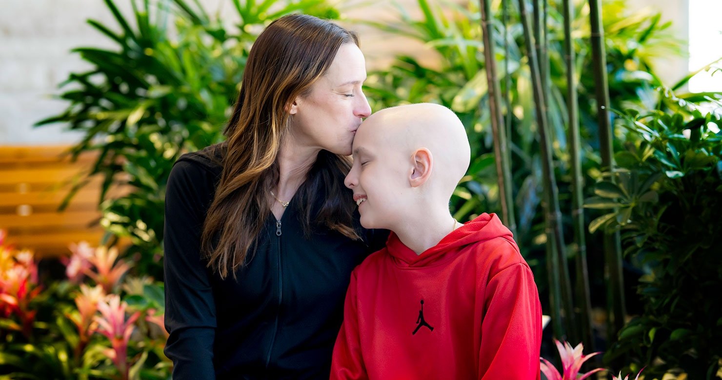 Woman kisses child on the head surrounded by green plants