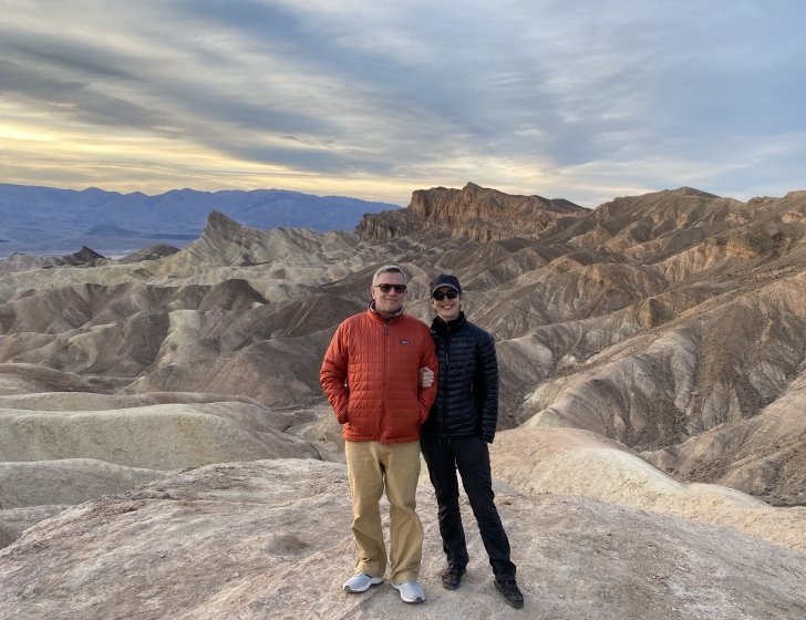 Stacey and husband stand on a boulder with mountains in the background