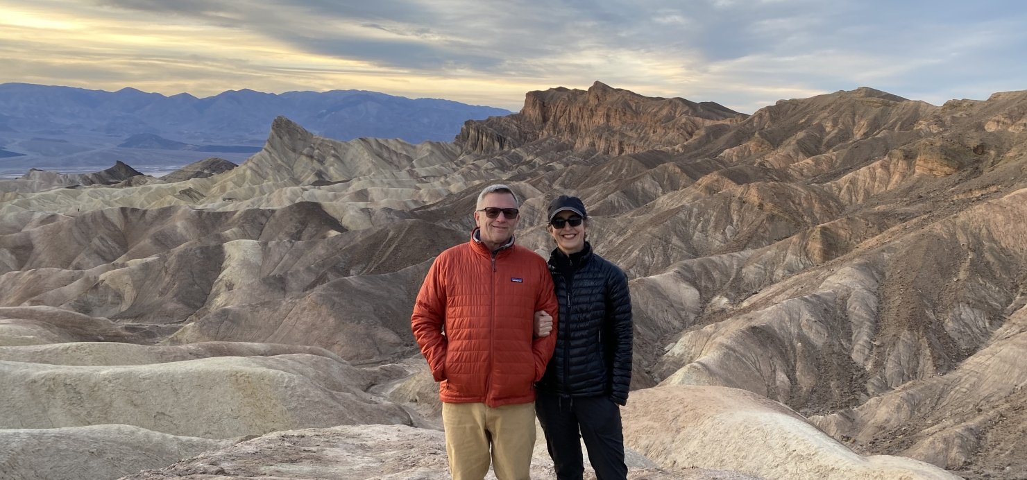 Stacey and husband stand on a boulder with mountains in the background