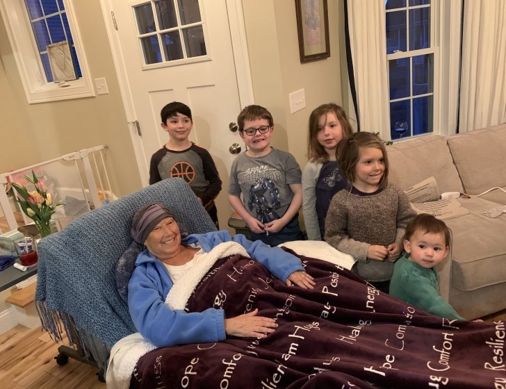 Joanna lies in bed in living room with five young children standing next to her