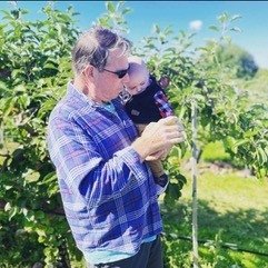 Al holds a baby while both look at a tree