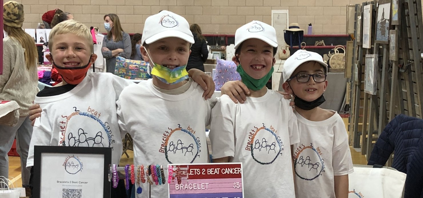 Four friends stand behind bracelet booth