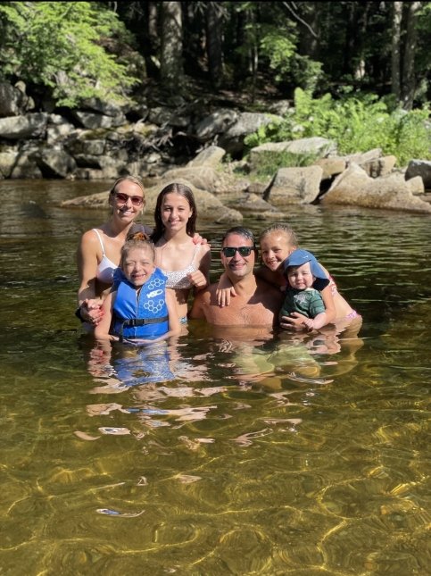 Family stands together in the water surrounded by trees