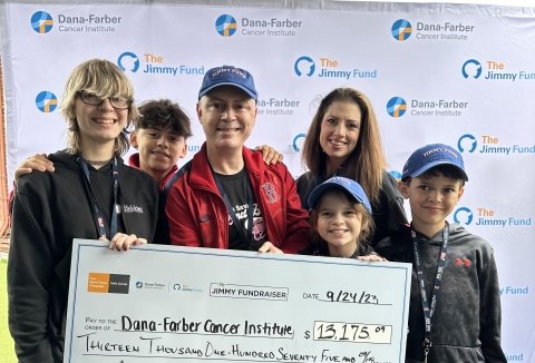 James and family hold large check in front of “The Jimmy Fund” backdrop