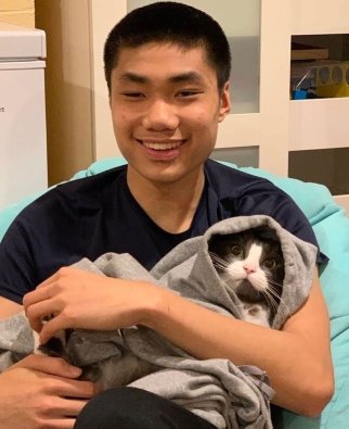 Amine sits in chair holding a cat wrapped in a sweatshirt