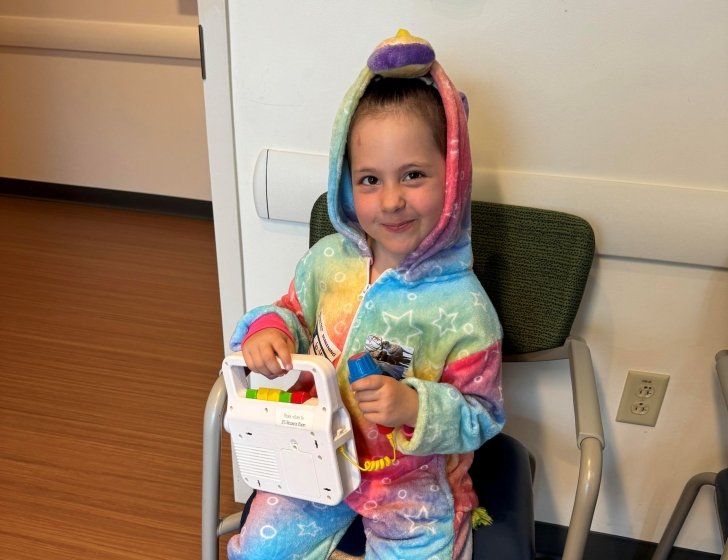 Sonnie in a chair with a toy in a rainbow outfit