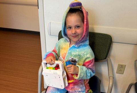 Sonnie in a chair with a toy in a rainbow outfit