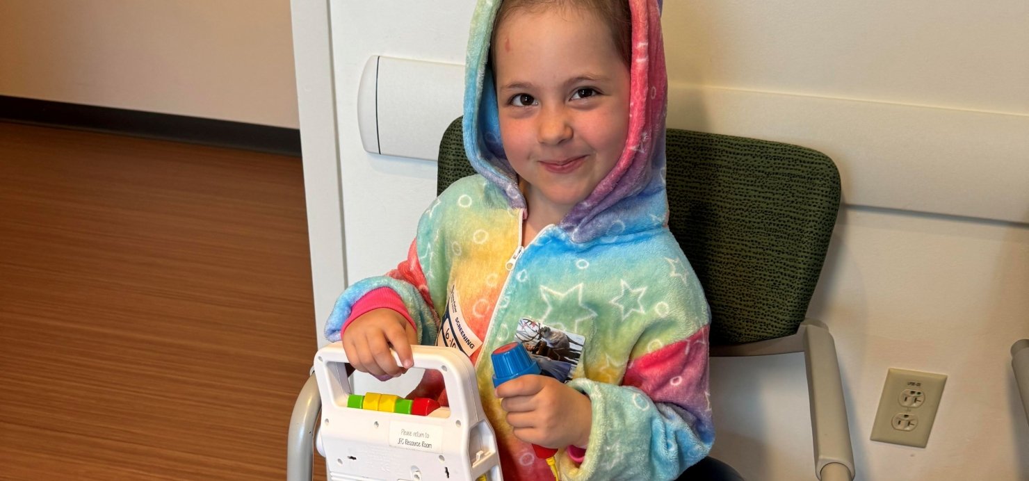 Sonnie in a chair with a toy in a rainbow outfit