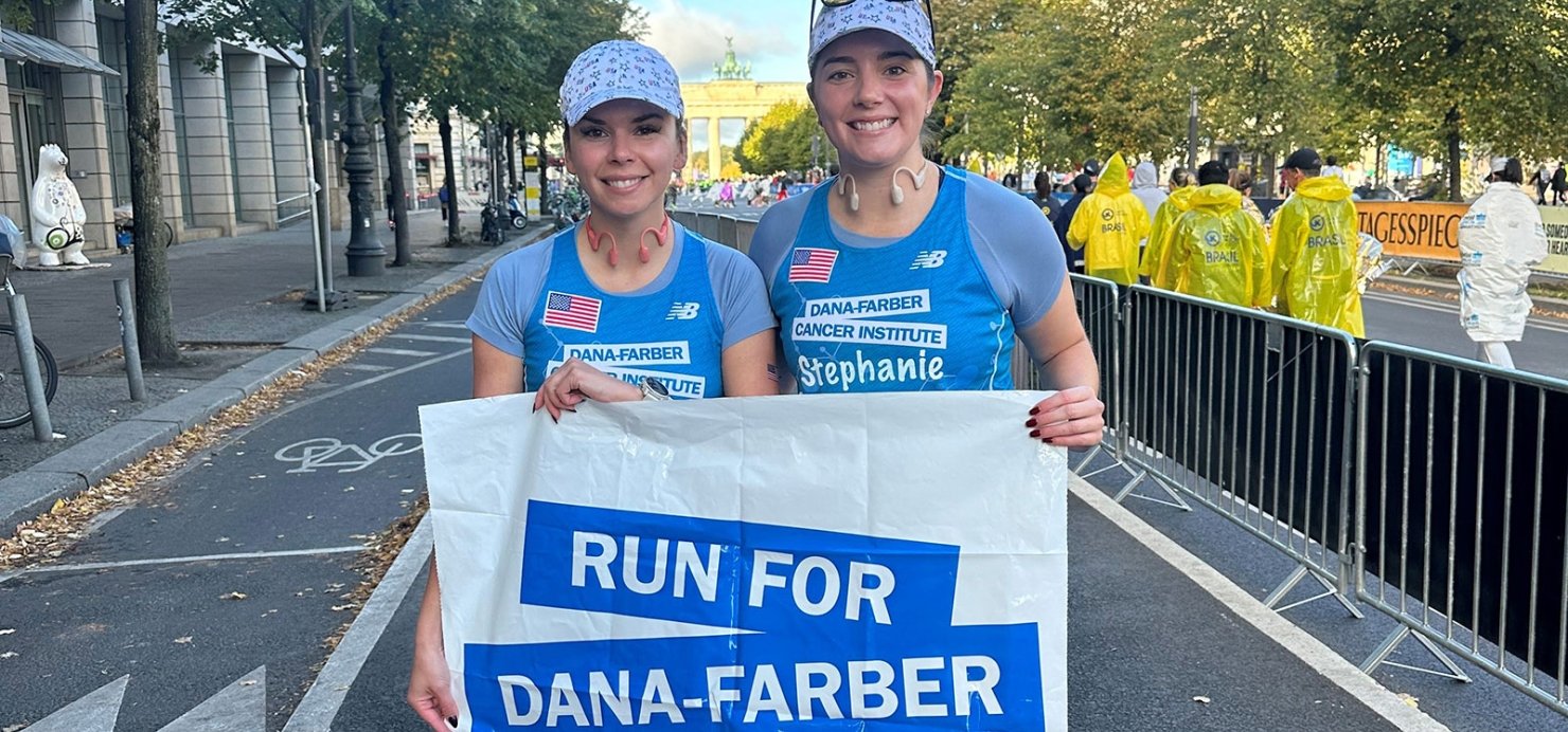 Kristina and Stephanie in their running gear holding a Run for Dana-Farber sign