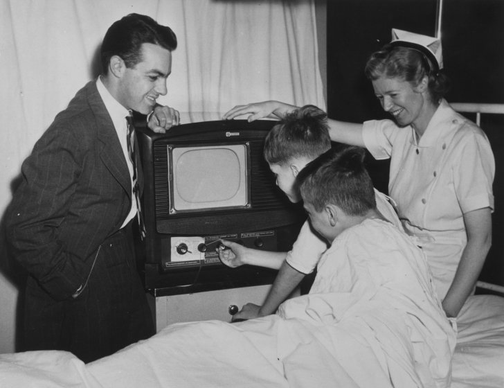 Black and white photo of children and adults with a TV