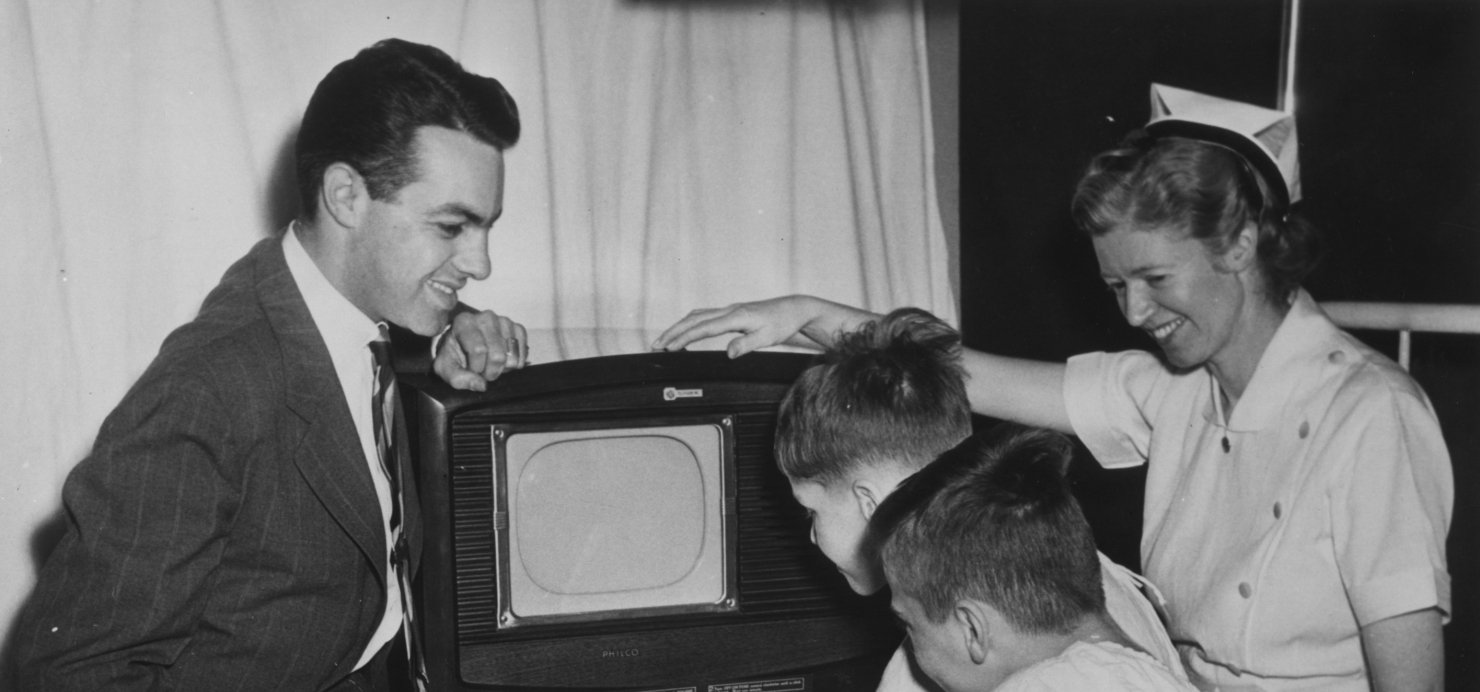 Black and white photo of children and adults with a TV