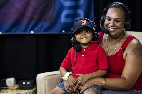 Woman and child sit in armchair, both wearing headphones and microphones