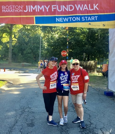 Three people stand together under 'Jimmy Fund Walk Newton Start' banner