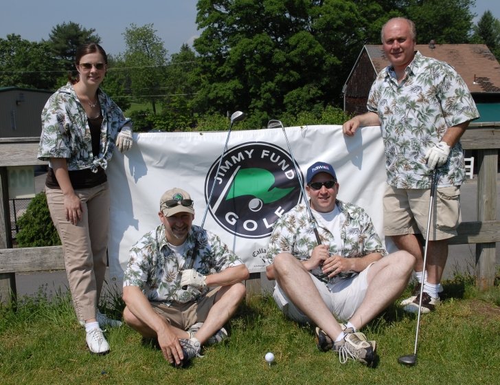 Family wears Hawaiian shirts and holds golf clubs in front of a Jimmy Fund Golf sign 