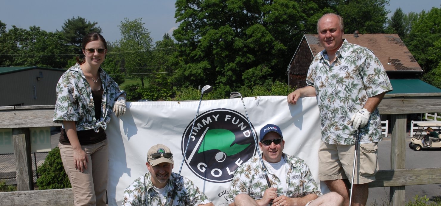 Family wears Hawaiian shirts and holds golf clubs in front of a Jimmy Fund Golf sign