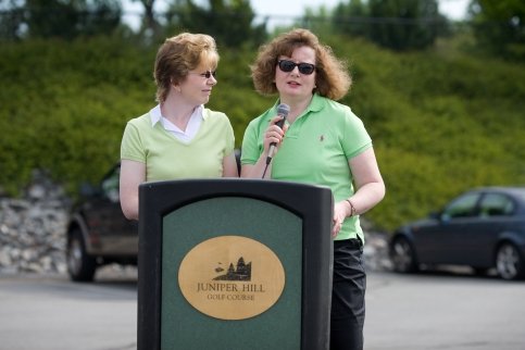 Lisa and Lynn stand at a podium that reads 'Juniper Hill Golf Course'