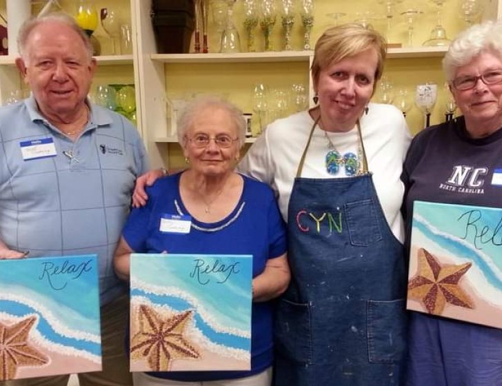 Cindy stands with three people holding up their paintings