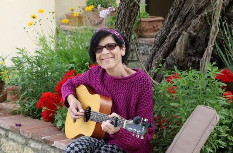 Patient sits on a stone wall playing guitar next to a garden