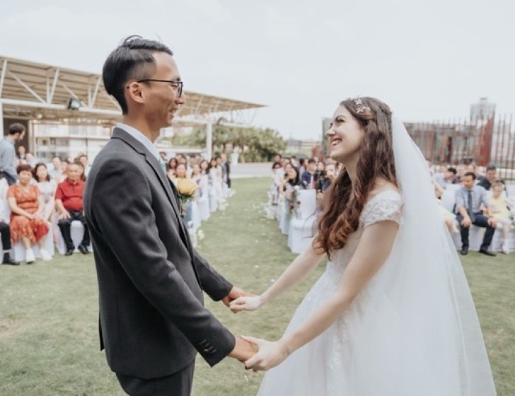 Husband and wife hold hands at wedding with family and friends watching