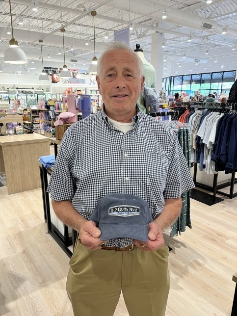 Larry in a clothing store holding a hat that says ‘Old Guys Rule’