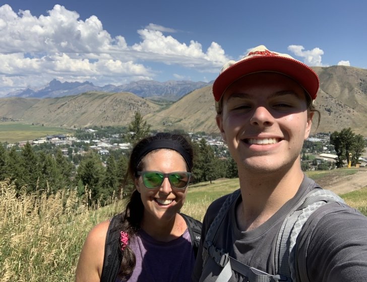 Marlene and son stand on a hiking trail with mountains in the background