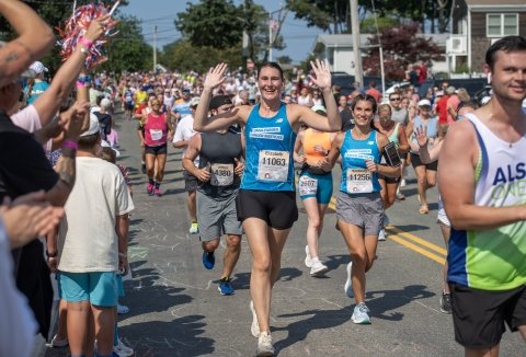 Elizabeth runs wearing a “Dana-Farber” singlet with arms in air