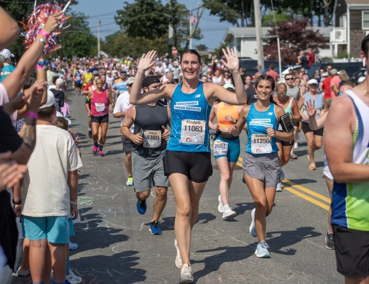 Elizabeth runs wearing a Dana-Farber singlet with arms in air