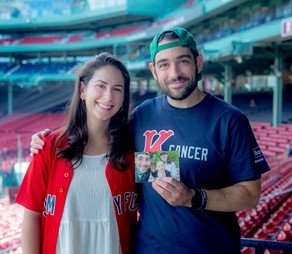 Rachel and Andrew stand in Fenway Park holding a family photo