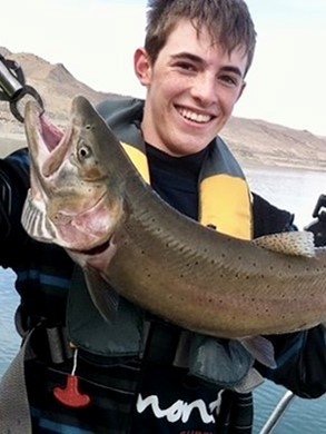 Max holds a fish while standing in a boat surrounded by water