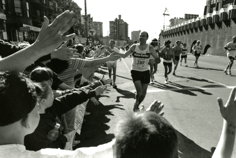 Black and white photo of a past DFMC runner high-fiving people in the crowd while running on the course