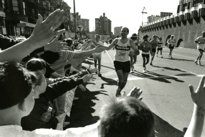 A black and white photo of a past DFMC runner high fiving people in the crowd while running on the course
