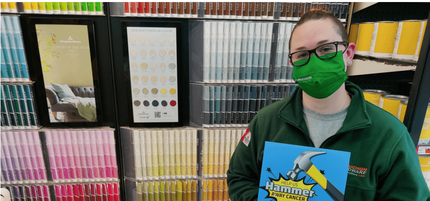 Leigh stands with 'Hammer Away' sign in front of paint samples wall
