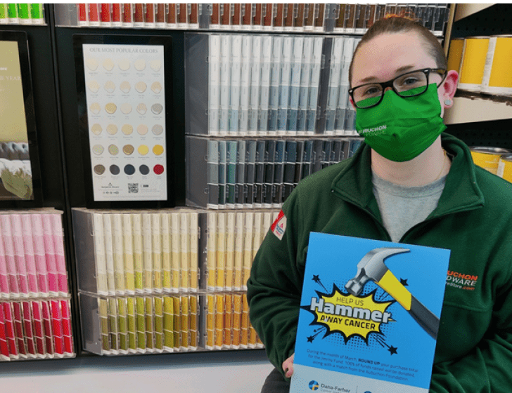 Leigh stands with 'Hammer Away' sign in front of paint samples wall
