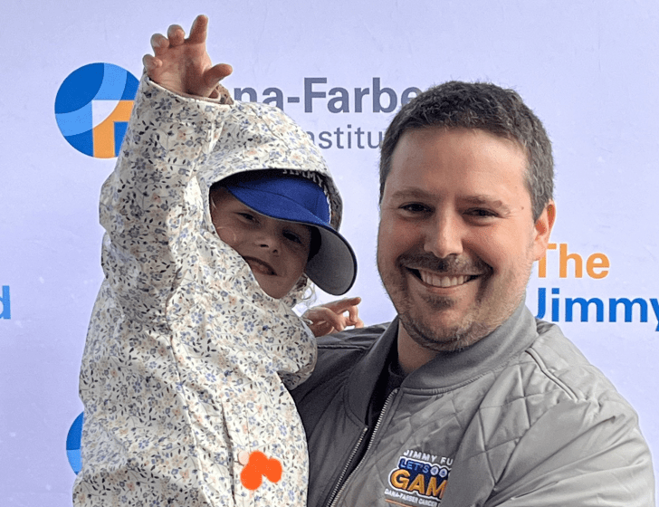 Dad holds child in front of Dana-Farber and the Jimmy Fund backdrop