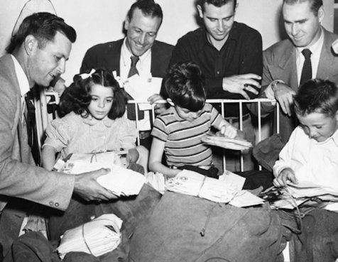 Black and white photo of children opening presents while adults look on and smile